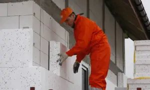 Budowlaniec w pomarańczowym stroju montuje płyty ze styropianu, dbając o niski lambda styropianu.