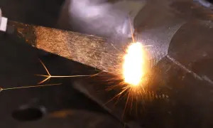 Jasny łuk spawalniczy rozświetla ciemność, sypiąc iskrami podczas spawania żeliwa.