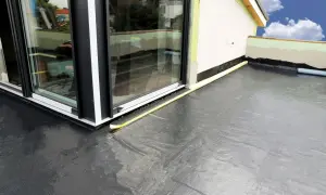 Nowoczesna hydroizolacja na balkon z czarnej membrany, zabezpieczająca przed wilgocią. Widoczny fragment budynku i okna.