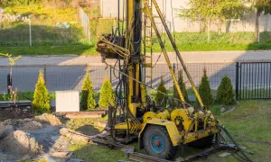Żółta wiertnica na podwórku, przygotowana do wiercenia studni głębinowej. Poznaj koszt takiej inwestycji.