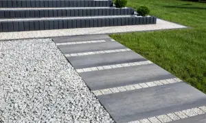 Nowoczesny chodnik z płyt betonowych i kamyczków, prowadzący do schodów.