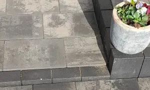 Różne rodzaje kostki brukowej tworzą elegancką ścieżkę. Jasnoszara i grafitowa kostka brukowa, z ozdobną donicą z kwiatami.