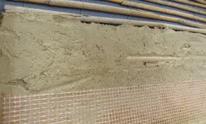 Warstwa tynków glinianych na bambusowym rusztowaniu, z siatką zbrojeniową u dołu.
