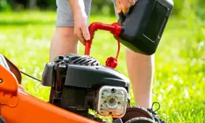 Mężczyzna nalewa paliwo do kosiarki. Czerwony lejek ułatwia zadanie, a czarny kanister czeka na uzupełnienie.