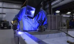 Spawacz w masce i rękawicach łączy metalowe elementy, pokazując, jak spawać migomatem.