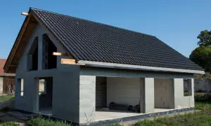 Dom w stanie surowym otwartym, z ciemnym dachem i betonowymi ścianami, czeka na dalsze prace.