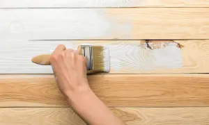 Ręka maluje białą farbą drewnianą boazerię, odświeżając jej wygląd.
