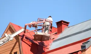 Pracownik na podnośniku maluje czerwony dach. Sprawdź, jaka jest malowanie dachu cena i odśwież wygląd swojego domu.