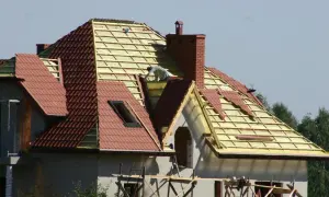 Budowa domu z czerwoną **attiką** i nowym dachem.