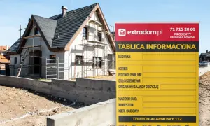 Tablica informacyjna budowy domu w trakcie prac. Widoczny dom w rusztowaniach i ogrodzenie.