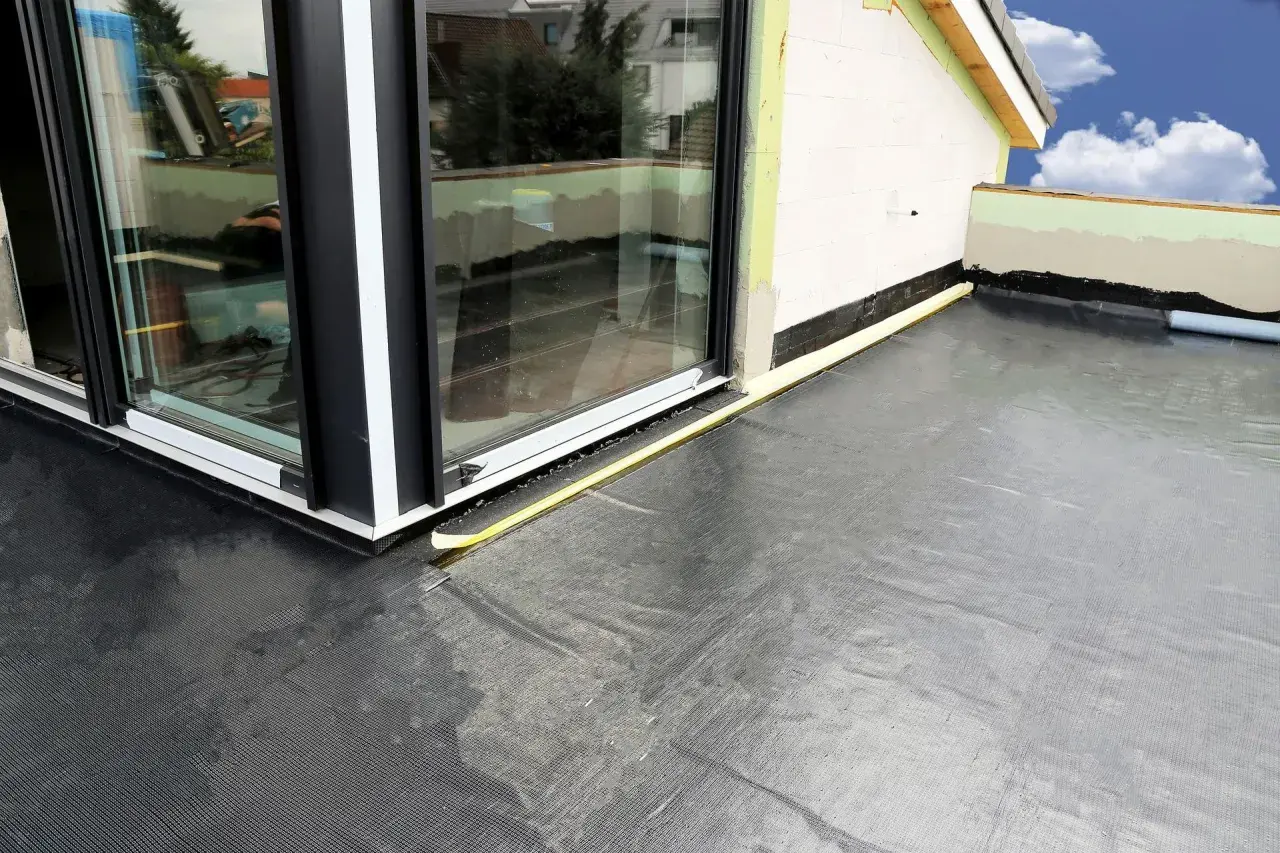 Nowoczesna hydroizolacja na balkon z czarnej membrany, zabezpieczająca przed wilgocią. Widoczny fragment budynku i okna.