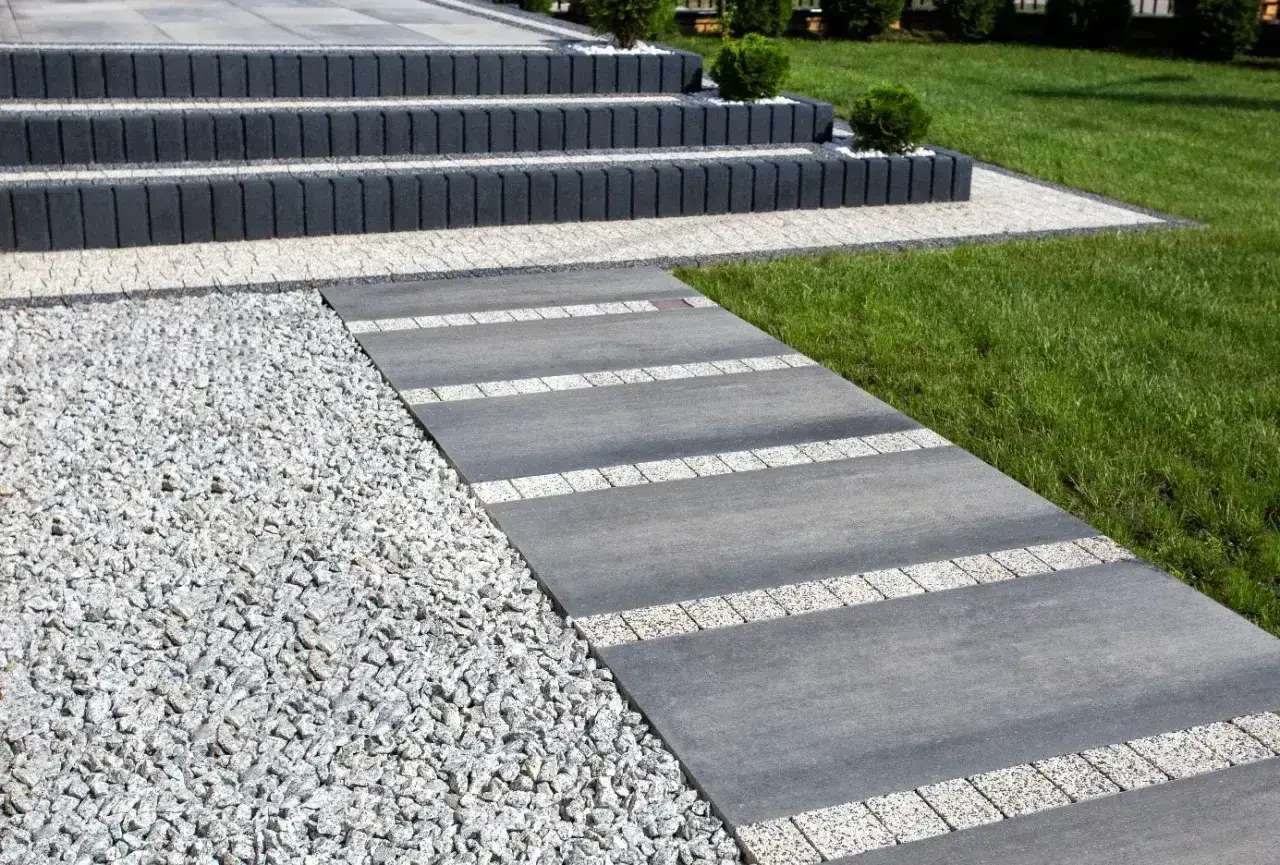 Nowoczesny chodnik z płyt betonowych i kamyczków, prowadzący do schodów.