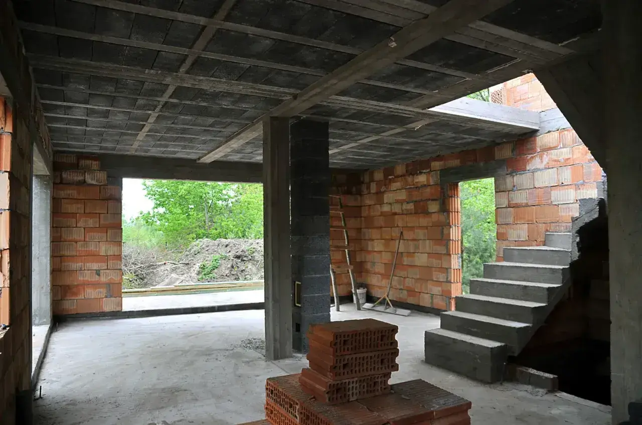 Wnętrze budowy z widocznym stropem monolitycznym, schodami betonowymi i ścianami z pustaków.