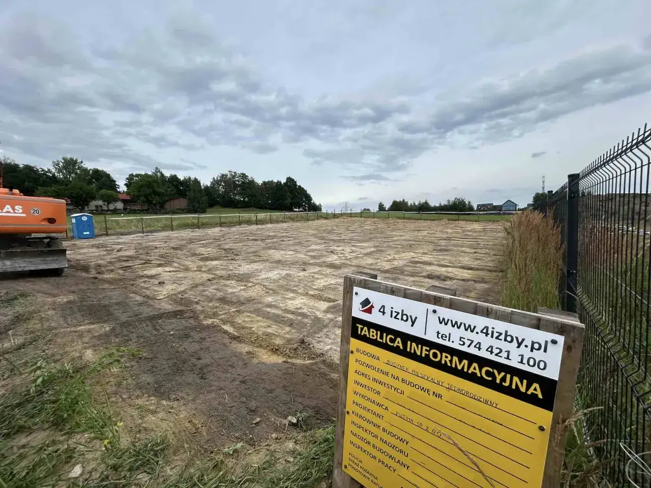 Tablica informacyjna budowy na placu budowy z koparką w tle.
