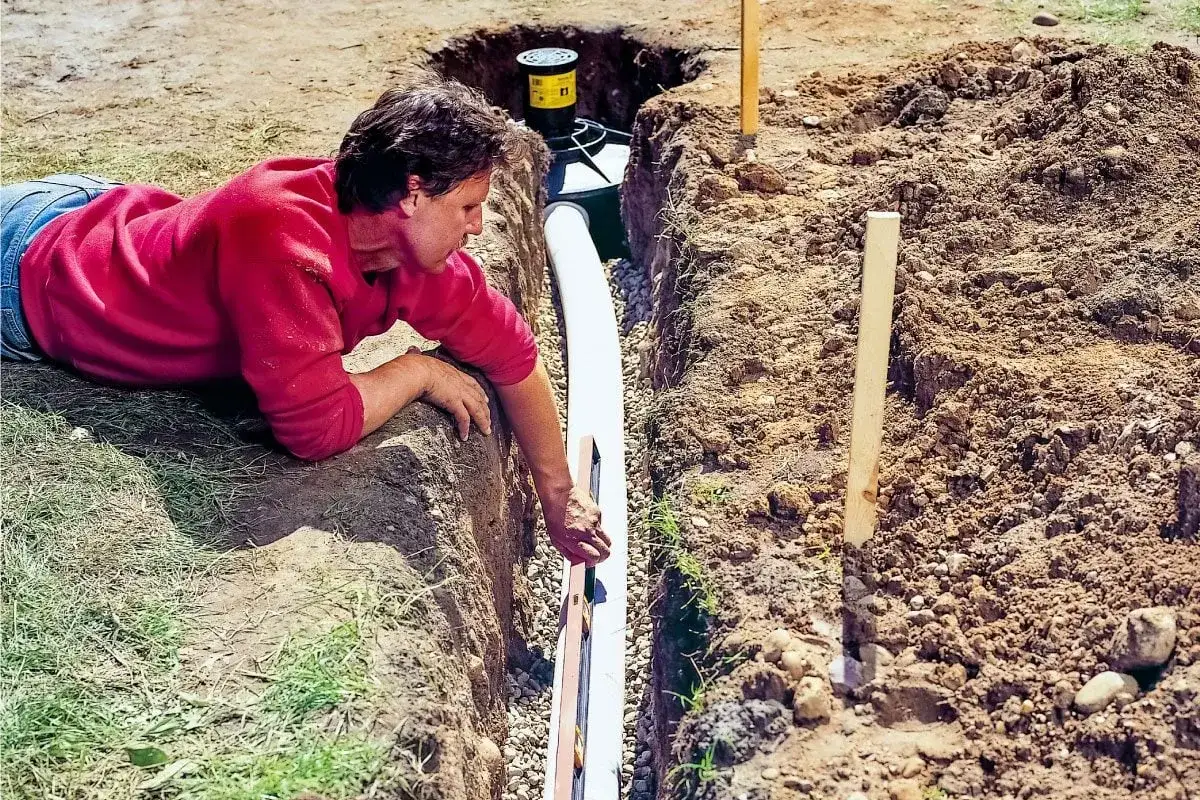 Mężczyzna układa rury do odprowadzenia wody z rynien. Wybór odpowiednich rur jest kluczowy dla skutecznego drenażu.
