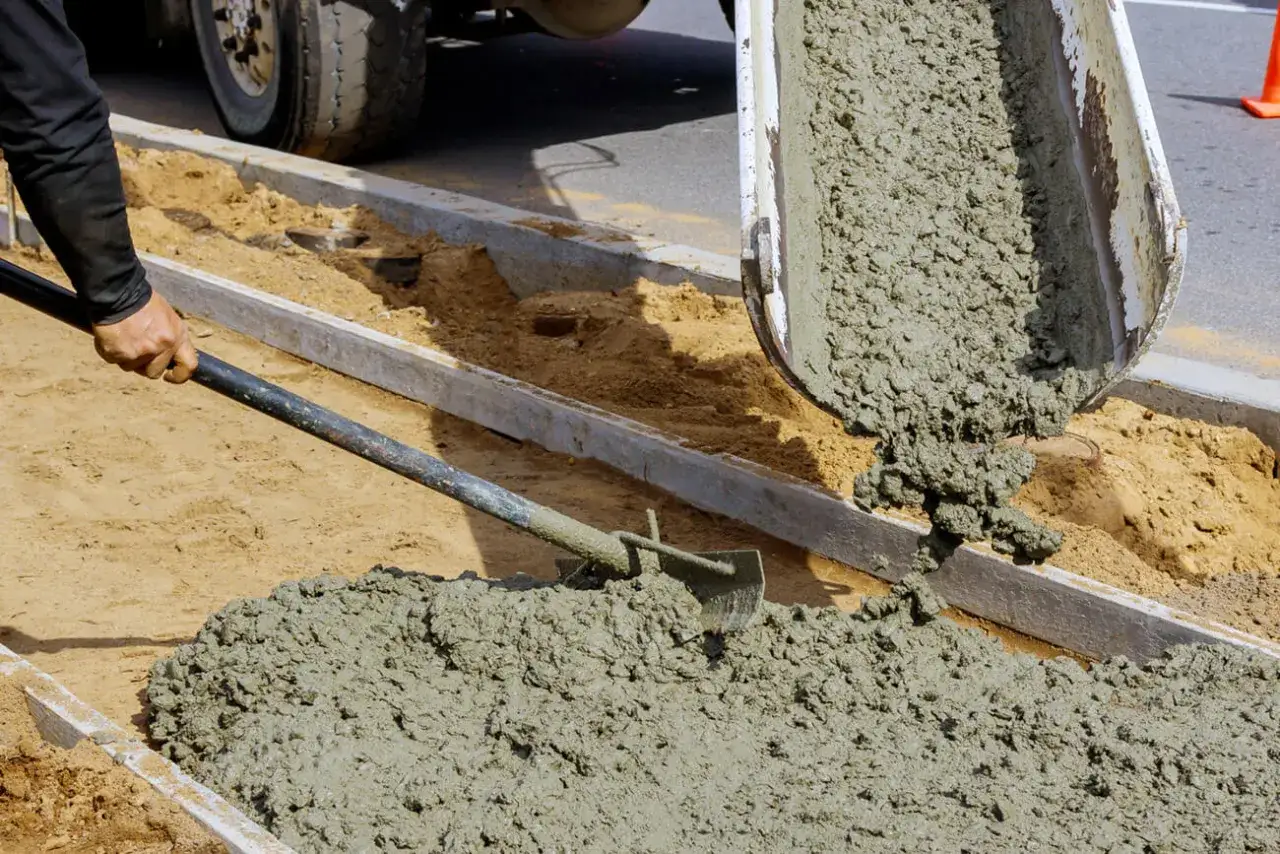 Praca przy budowie chodnika. Wylewanie betonu z betoniarki. Ile cementu na 1m3 betonu? To kluczowe pytanie przy tworzeniu trwałej konstrukcji.