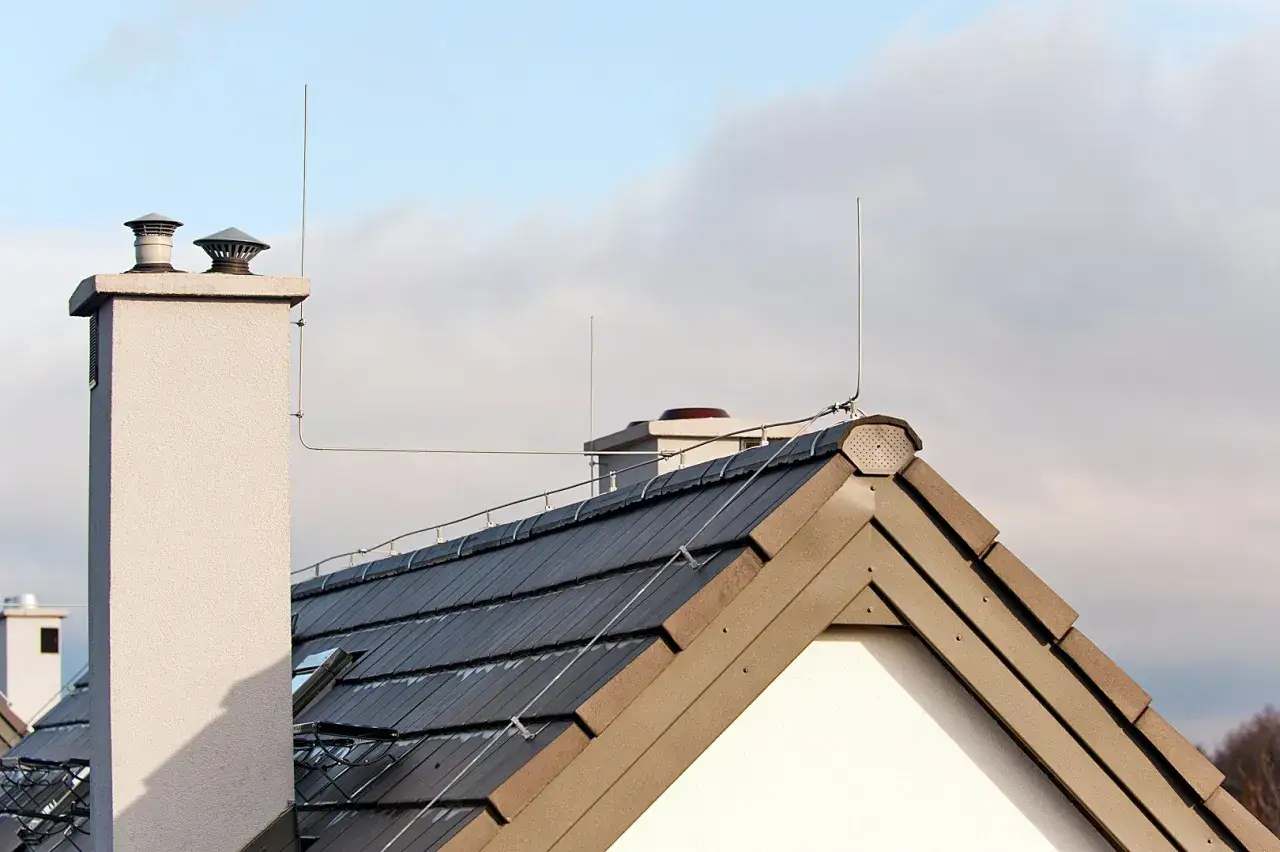 Dach z dachówką i kominem, na którym widoczna jest instalacja odgromowa chroniąca budynek przed wyładowaniami atmosferycznymi.