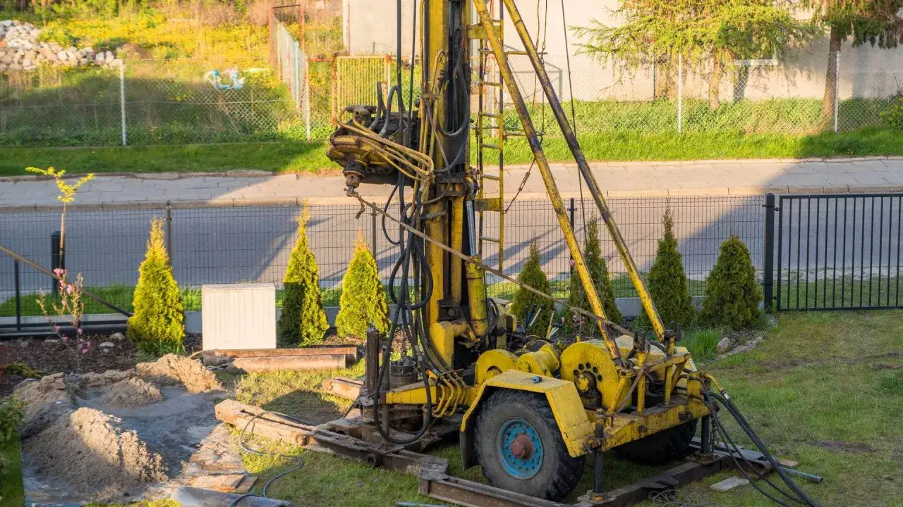 Żółta wiertnica na podwórku, przygotowana do wiercenia studni głębinowej. Poznaj koszt takiej inwestycji.