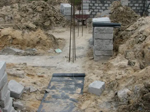 Budowa domu w toku. Widać wykopy, zbrojenie i materiały budowlane. To dopiero początek prac nad fundamentem.