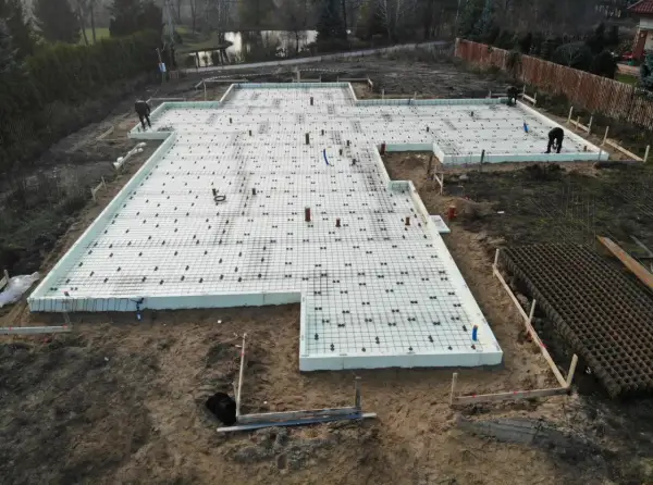 Przygotowania do wylania fundamentów pod garaż. Na placu budowy widać styropian, zbrojenie i elementy instalacji.