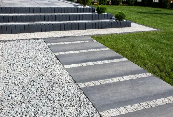 Nowoczesny chodnik z płyt betonowych i kamyczków, prowadzący do schodów.