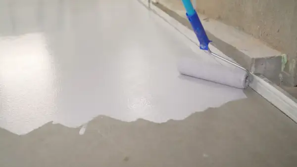 Wałek maluje beton na biało, tworząc gładką, jednolitą powierzchnię.