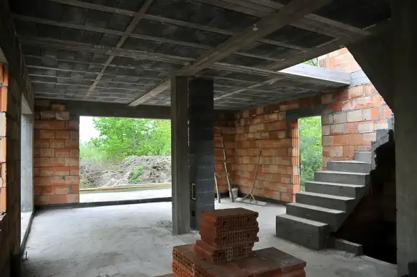 Wnętrze budowy z widocznym stropem monolitycznym, schodami betonowymi i ścianami z pustaków.