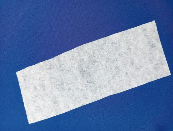 Biała flizelina na granatowym tle. Materiał jest lekko pofałdowany, tworząc subtelne cienie.