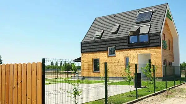 Nowoczesny dom z drewnianą elewacją i panelami słonecznymi na dachu. To ekologiczne rozwiązanie, przypominające trochę earthship, z pewnością przyciąga wzrok.
