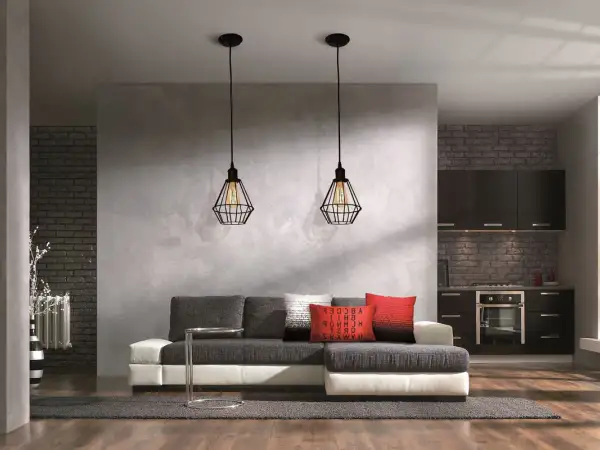 Nowoczesna ściana działowa z betonową fakturą oddziela salon od kuchni. Dwa industrialne lampy wiszące nad kanapą.