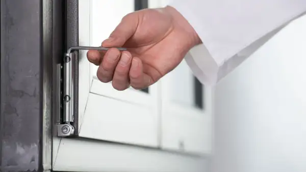 Dłoń z kluczem imbusowym reguluje zawias okna. Przygotowanie do trybu zimowego regulacja okien na zimę.