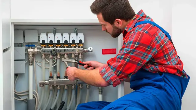 Instalator dokręca kluczem rurę w rozdzielaczu ogrzewania podłogowego.
